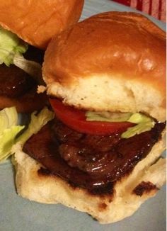 two hamburgers with meat, lettuce and tomato on them sitting on a plate