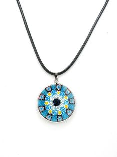 From the Italian for "thousand flowers," Millefiori jewelry is famous for its beautiful and intricate designs. This authentic round Millefiori necklace features bright shades of blue colors in a mosaic pattern. The black cord necklace measures about 18", with a silver-plated clasp. The pendant rim and necklace clasp are also silver-plated. At 1 1/4", the glass pendant is sizable and sure to make a statement. Because no two necklaces are exactly alike, yours may be slightly different than the one Flower Pendant Necklace With Adjustable Cord, Adjustable Blue Medallion Necklace, Blue Flower Pendant Necklace With Large Pendant, Adjustable Blue Flower Pendant Necklace, Blue Round Pendant Necklace, Adjustable Blue Round Pendant Necklace, Blue Necklace With Round Pendant, Adjustable, Blue Necklace With Adjustable Cord As Gift, Blue Adjustable Cord Necklace For Gift