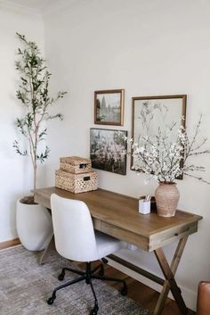 a wooden desk topped with a white chair next to a potted plant and framed pictures