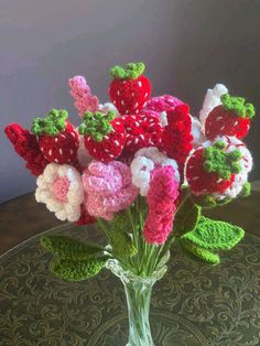 crocheted strawberries and flowers in a glass vase on a round table top