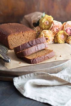 sliced loaf of bread sitting on top of a wooden cutting board next to some flowers