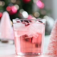 a glass filled with ice and cranberries on top of a table next to a christmas tree