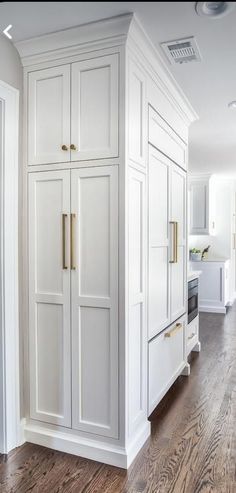 a white kitchen with wood floors and cabinets in the center, along with an oven