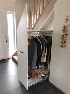 an open closet under the stairs with clothes hanging on hooks and shoes in front of it