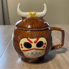 a ceramic mug with a mask painted on the side and horns sticking out of it