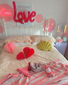 a bed with pink and white sheets, pillows and decorations on top of it in front of a love sign