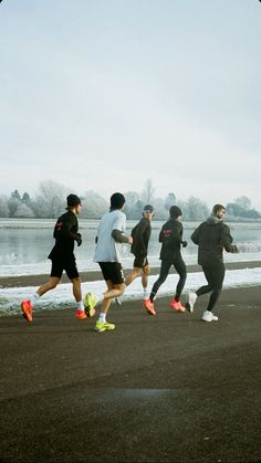 a group of people running down a street next to the water with snow on the ground