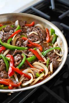 a skillet filled with beef, peppers and onions on top of an oven burner