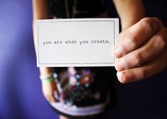 a person holding up a card with the words you are what you create