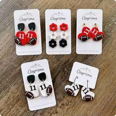 four pairs of earrings with footballs on them sitting on top of a wooden table