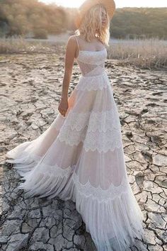 a woman in a white dress and hat standing on dry land with her back to the camera