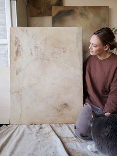 a woman sitting on top of a bed next to a gray and white cat near a painting