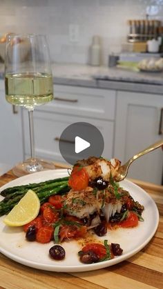 a white plate topped with fish and vegetables next to a glass of wine on top of a wooden table