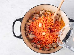 a pot filled with carrots and meat next to a wooden spoon