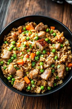 a bowl filled with rice, peas and meat on top of a wooden table next to a fork