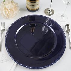 there is a blue plate and silverware on the table next to a bottle of wine