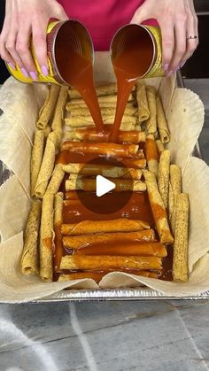 a person pouring sauce on french fries in a pan with tinfoil wrappers around them