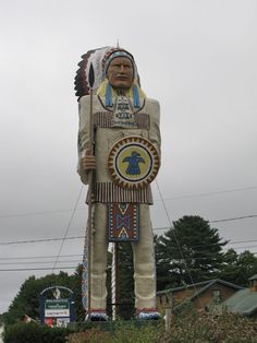 a large statue of a native american standing in front of a sign for the entrance to an amusement park