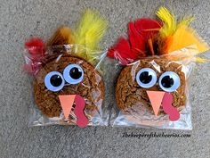 two turkey cookies wrapped in plastic with fake eyes and feathers on them, sitting next to each other