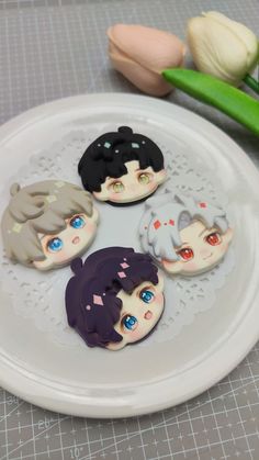 four decorated cookies sitting on top of a white plate next to tulips and flowers