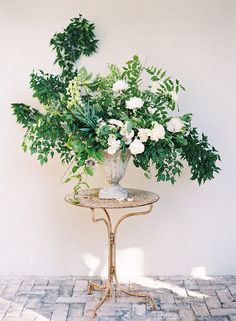 a vase filled with white flowers sitting on top of a table next to a wall