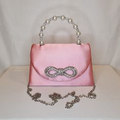 Womens pink top handle evening clutch bag with crystal bow embellishment, crystal and pearl detailed top handle, satin finish material and magnet front closing clasp Can be used with or without long shoulder chain (included) size approx- H 13cm x W 20cm Optional Dust Bag: White lightweight soft polyester portable travel dust bag pouch, suitable for protecting items from dust, dirt, hairs and scratches when not in use size approx- L 47cm x W 31.5cm Material: 100% polyester Please note, there is a Elegant Wedding Bags With Bow Detail, Elegant Wedding Bags With Bow, Pink Rhinestone Clutch For Evening, Feminine Rectangular Evening Bag For Party, Pink Chic Evening Bag For Formal Occasions, Elegant Bags With Bow For Events, Elegant Evening Bags With Satin Bow, Elegant Party Bag With Satin Bow, Glamorous Pink Handheld Evening Bag