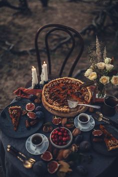 a table topped with a pie covered in toppings next to candles and plates filled with food