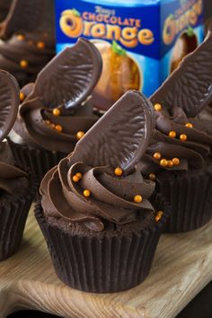 chocolate cupcakes with orange frosting on a cutting board next to a carton of orange juice