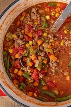 a pot filled with soup and vegetables on top of a wooden table next to a spoon