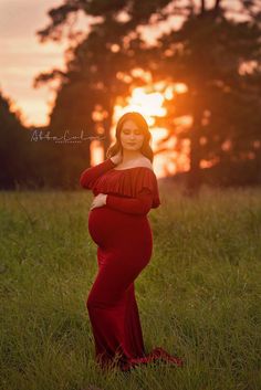 a pregnant woman in a red dress poses for a photo at sunset with her hands on her belly