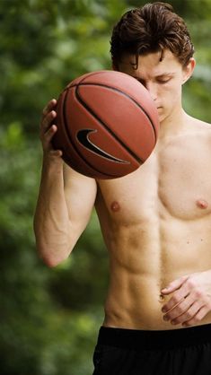 a shirtless man holding a basketball in his right hand and looking down at it