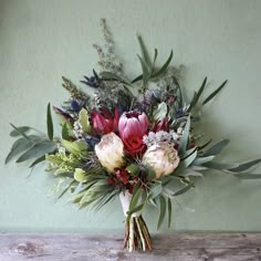 a bouquet of flowers sitting on top of a wooden table next to a green wall