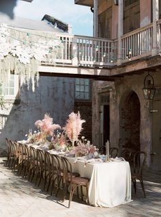 an outdoor dining table set up with pink flowers and candles on it in front of a building