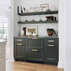 a kitchen with gray cabinets and gold pulls on the countertop, along with white walls