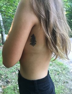 the back of a woman's shoulder with a small pine tree tattoo on it