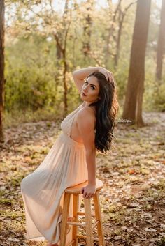 a beautiful woman sitting on top of a wooden stool in the middle of a forest