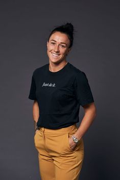 a woman in black shirt and tan pants smiling at the camera with her hands on her hips