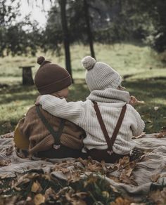 two toddlers sitting on a blanket in the woods, one holding his back to the camera