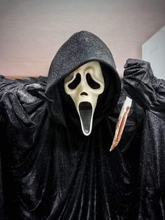 a person in a black hooded costume with a book sticking out of their mouth and wearing a scream mask