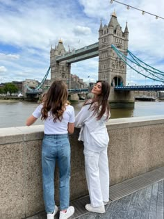 two girls standing on the side of a bridge looking up at the tower of london