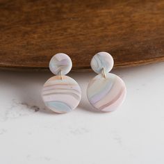 two white and pink marbled earrings on a wooden platter next to a piece of wood