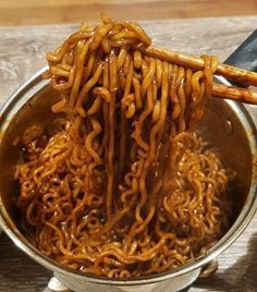 a ladle full of noodles being held by chopsticks