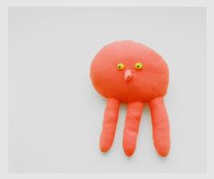 an orange stuffed animal with green eyes on it's head and arms, sitting in front of a white background