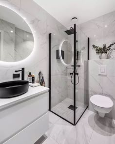 a white bathroom with marble walls and flooring is pictured here in this image, there is a round mirror on the wall above the shower