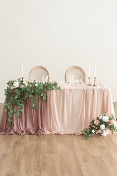 the table is set with two chairs and pink drapes on it, along with greenery