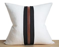 a white pillow with black and brown stripes on the front, sitting on a wooden table