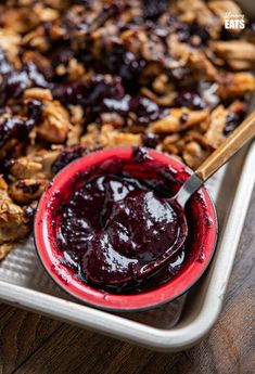 a red bowl filled with blueberry sauce next to granola on a white tray