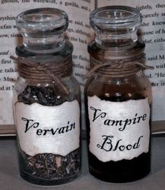 two glass bottles with labels on them sitting next to an open book that reads, vampire blood