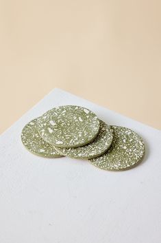 three green coasters sitting on top of a white cloth covered tablecloth in front of a beige wall