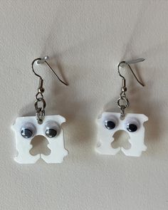 pair of white earrings with black eyes and dog face on each earring, hanging from hooks